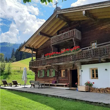 Ein charmantes Holzhaus mit Balkonen und Blumenkästen. Es liegt in einer grünen Landschaft unter einem klaren blauen Himmel.