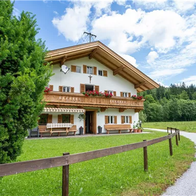 A charming country house with a balcony and blooming flowers. It is situated in a green environment with clouds in the blue sky.