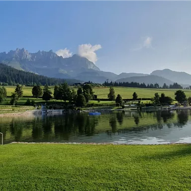A picturesque lake surrounded by green meadows and mountains. The sky is clear, and the landscape radiates tranquility.