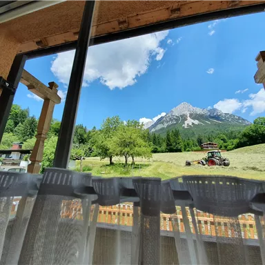 A beautiful view from the window of the mountains and a green meadow. In the foreground, a tractor is seen working in the landscape.