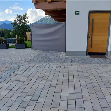 A paved entrance area with a wooden door and a privacy screen. In the background, trees and mountains are visible.