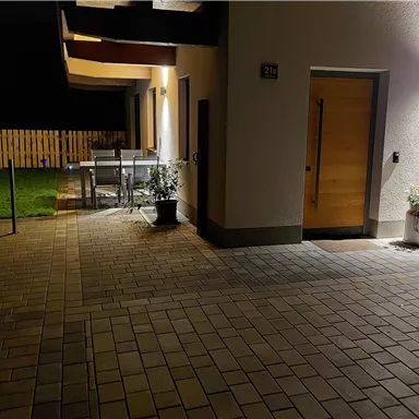 A modern entrance area with a paved surface. In the background, garden furniture and a lawn are visible.