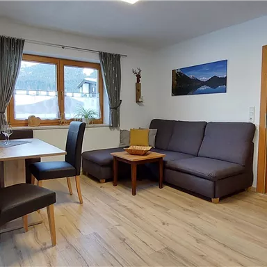 A cozy living space with a dining area and a sofa corner. Large windows bring plenty of daylight and offer a view of the surroundings.