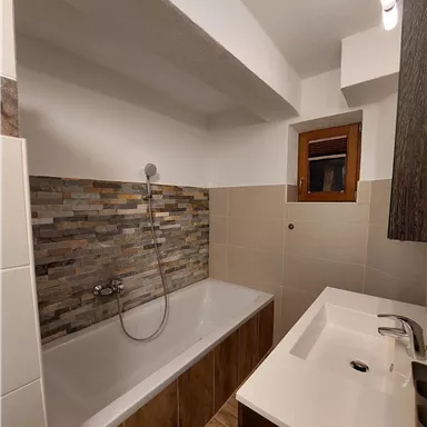 Ein modernes Badezimmer mit einer Badewanne und einem Waschbecken. Die Wände sind teilweise mit dekorativen Fliesen gestaltet.
