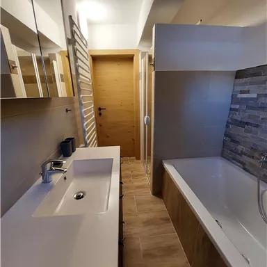 Ein modernes Badezimmer mit einem Waschbecken, einer Badewanne und eleganten Holz- und Fliesenelementen. Viel Licht strahlt durch den Raum und sorgt für eine einladende Atmosphäre.