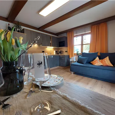 A cozy apartment with a modern kitchen and an inviting living area. Fresh flowers and a set table decor create a friendly atmosphere.