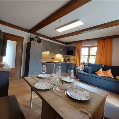 A modern living room with a cozy sofa and a dining table. The large window front provides plenty of daylight and an inviting atmosphere.
