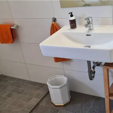 A modern bathroom with a sink, towels in orange, and a shower. The room is designed to be bright and friendly.