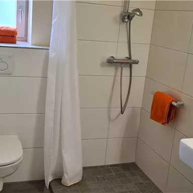 A modern bathroom with a shower and a white sink. Towels in orange and a bright, minimalist design create a friendly atmosphere.