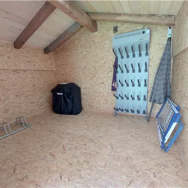 Ein leerer Raum mit holzverkleideten Wänden und einem hohen Dach. Auf der linken Seite befinden sich einige Aufhängemöglichkeiten und ein Grill.