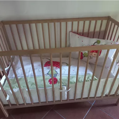 A wooden children's bed with a padded pillow and a blanket. The bedding has a cheerful strawberry pattern.