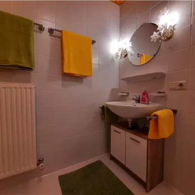 A modern bathroom with a sink and a round mirror. Colorful towels in yellow and green add color to the room.