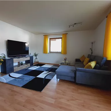 A modern living room with a large television and a cozy sofa. Yellow curtains and a stylish carpet create an inviting atmosphere.