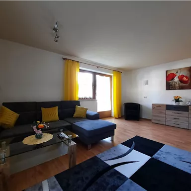 A modern living room with a gray sofa and yellow curtains. The room has a wooden floor and a stylish rug, as well as a small floral decoration.