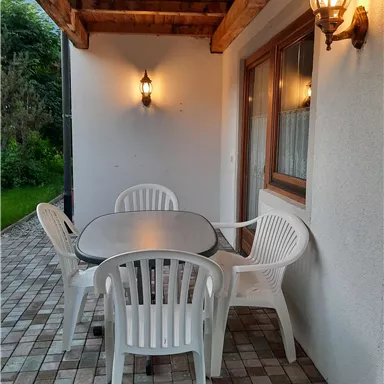 A cozy outdoor area with a table and four plastic chairs. The soft lighting creates a relaxed atmosphere.