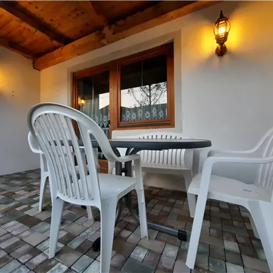 A cozy outdoor area with a table and two chairs. The walls are light, and there are wall lamps that create a pleasant atmosphere.