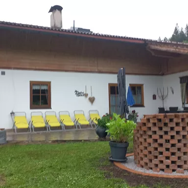 A traditional house with a wooden porch and a garden.  
In front of the house are yellow loungers and potted plants.