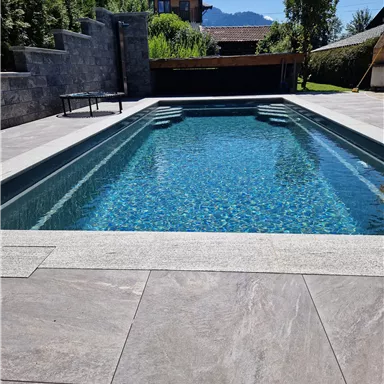 A stylish pool with clear blue water in a modern garden. Surrounded by nature and an appealing terrace area.