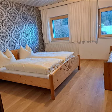 A cozy bedroom with two wooden beds and a window that offers a view of nature. The walls are decorated with an elegant pattern.