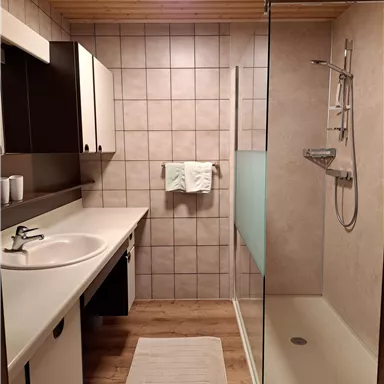 A modern bathroom with a large shower and a sink. The room has bright tiles and a wooden ceiling.