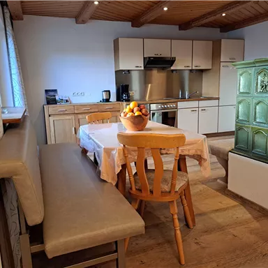 A cozy kitchen with a wood stove and a dining table. There is a bowl of fresh fruit on the table.