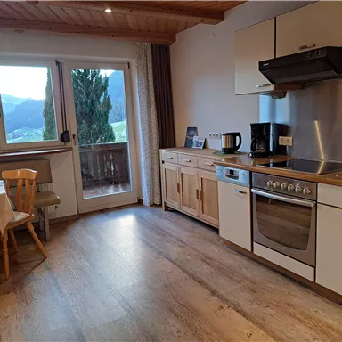A modern kitchen with wood details and a window that offers a view of the mountains. The room is bright and inviting, featuring a small dining table and chairs.