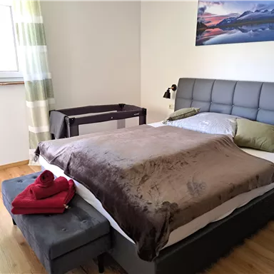 Ein modernes Schlafzimmer mit einem großen Bett und einer gemütlichen Bettdecke. Ein Stuhl und ein Tisch ergänzen die einfache, elegante Einrichtung.