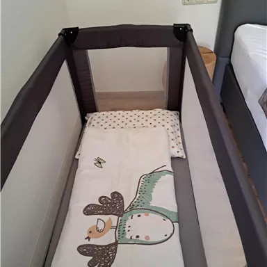 A baby bed with a colorful duvet cover and a mattress. The room looks bright and modern.