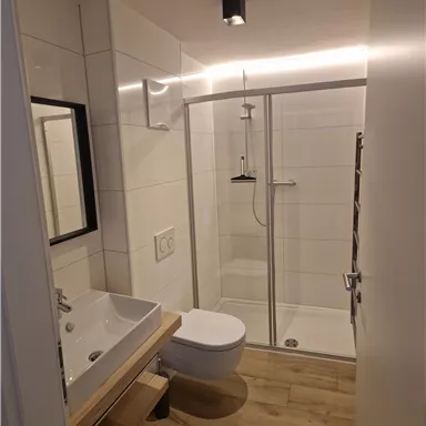 Ein modernes Badezimmer mit einer Glasdusche und hellem Fliesenboden. Ein Waschbecken und ein WC sind ebenfalls vorhanden.