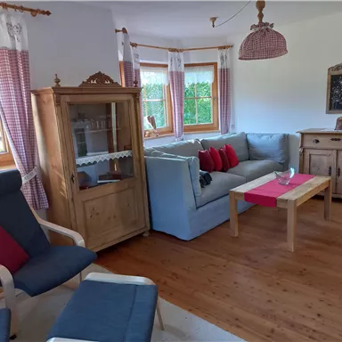 A cozy living room couch with red cushions and a wooden table. The room is bright and inviting, with large windows and wooden furniture.
