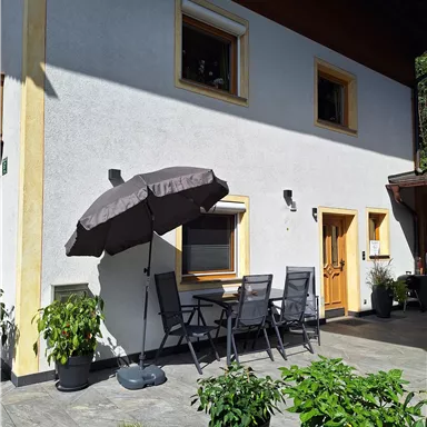 A beautiful house with a terrace and modern seating furniture. The garden is green and well-maintained with numerous plants.