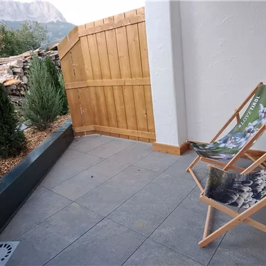 A quiet balcony with two lounge chairs and a view of the mountains. The surroundings are filled with green plants.