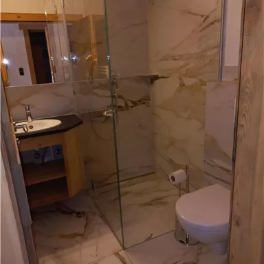 A modern bathroom with elegant marble tiles. There is a glass shower, a sink, and a toilet.