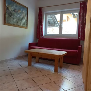 A simple living room with a red sofa and a wooden table.  
Large windows let in plenty of light and give the room a friendly atmosphere.