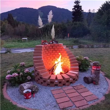 A cozy campfire area made of bricks with a burning fire. Surrounded by flowers and grasses, it offers a warm atmosphere in nature.