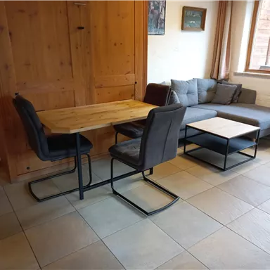 A cozy living area with a wooden studio table and stylish chairs. A gray couch and a side table are also in the room.