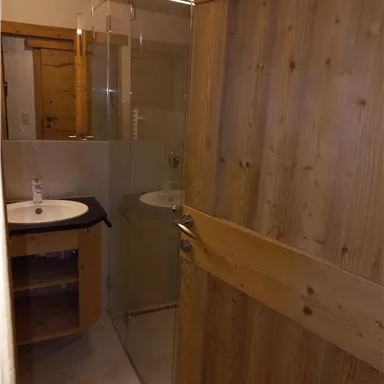 A modern bathroom with a glass shower and a wooden sink. The walls are bright and the floor is decorated.