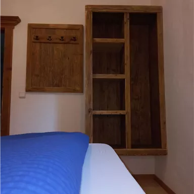 A cozy room with a bed and a wooden shelf on the wall. Next to the shelf is a wooden coat rack.
