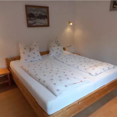 A cozy bedroom with a large double bed and two nightstands. The walls are light, and there is soft lighting.