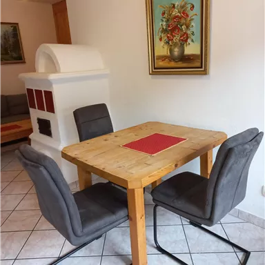 A cozy dining area with a wooden table and two gray chairs. A flower picture hangs on the wall, and in the background, there is a fireplace.