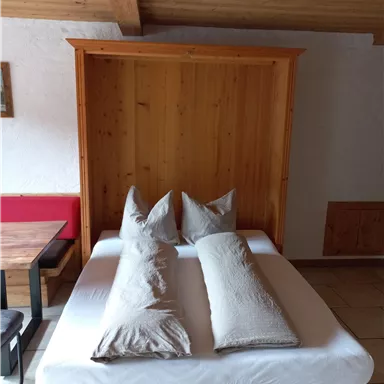 A cozy bedroom with a folding wooden bed and two pillows. The decor is simple and inviting.