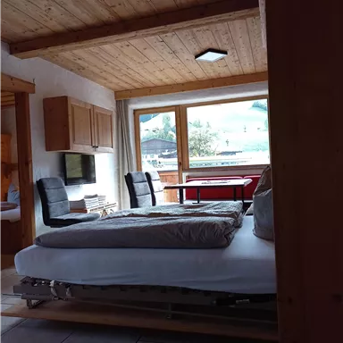 A cozy room with a bed and two chairs. Large windows provide plenty of light and a view of the landscape.