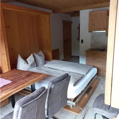 A cozy room with a bed, a dining table, and chairs. The walls are made of wood, and there is a small kitchenette.