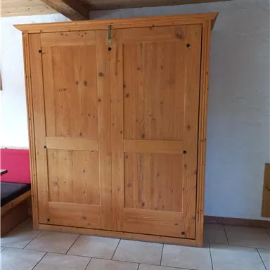 A large wooden cabinet with a double-door design stands in a room. The floor is laid with beautiful tiles.