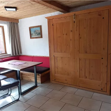 A cozy room with a table and chairs.  
On the wall stands a wooden cabinet and a window with a view.