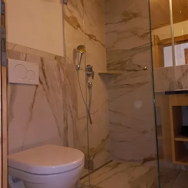 A modern bathroom with a glass shower enclosure and elegant marble tiles. A toilet is also available, complementing the space.