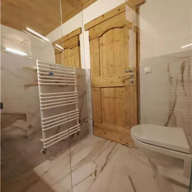 A modern bathroom with marbled tiles and a glass shower. Two wooden doors and a metal towel holder are clearly visible.