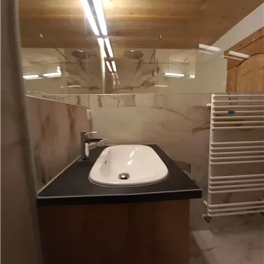 A modern bathroom with an elegant sink and wooden furniture. The walls are tiled with light marble and there is a towel radiator.