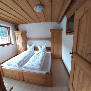 A bright bedroom with wood paneling. The bed has two single mattresses and there are two wardrobes.