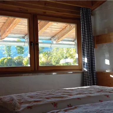 A cozy bedroom with a bed and a window that offers a view of nature. Bright sunlight streams through the window and illuminates the room.